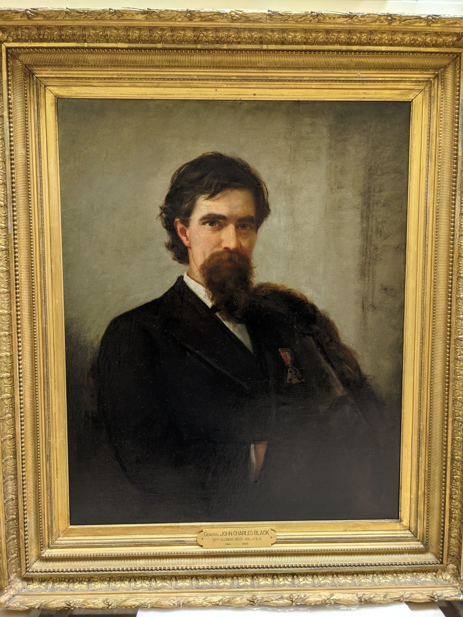 Portrait of John Black sitting down inside a gold frame.