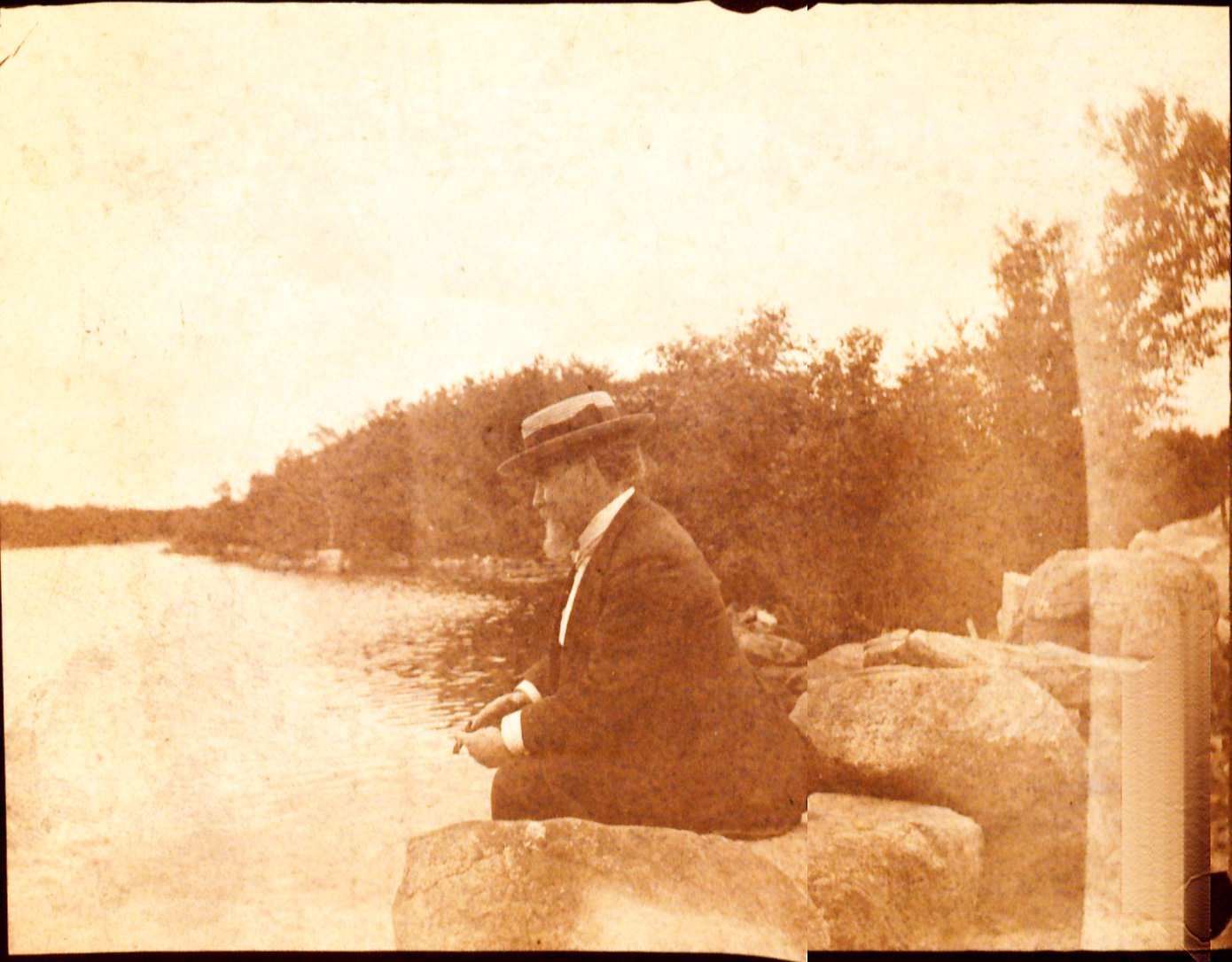 Picture of John Black sitting on a rock at a lake. there are trees surrounding the lake