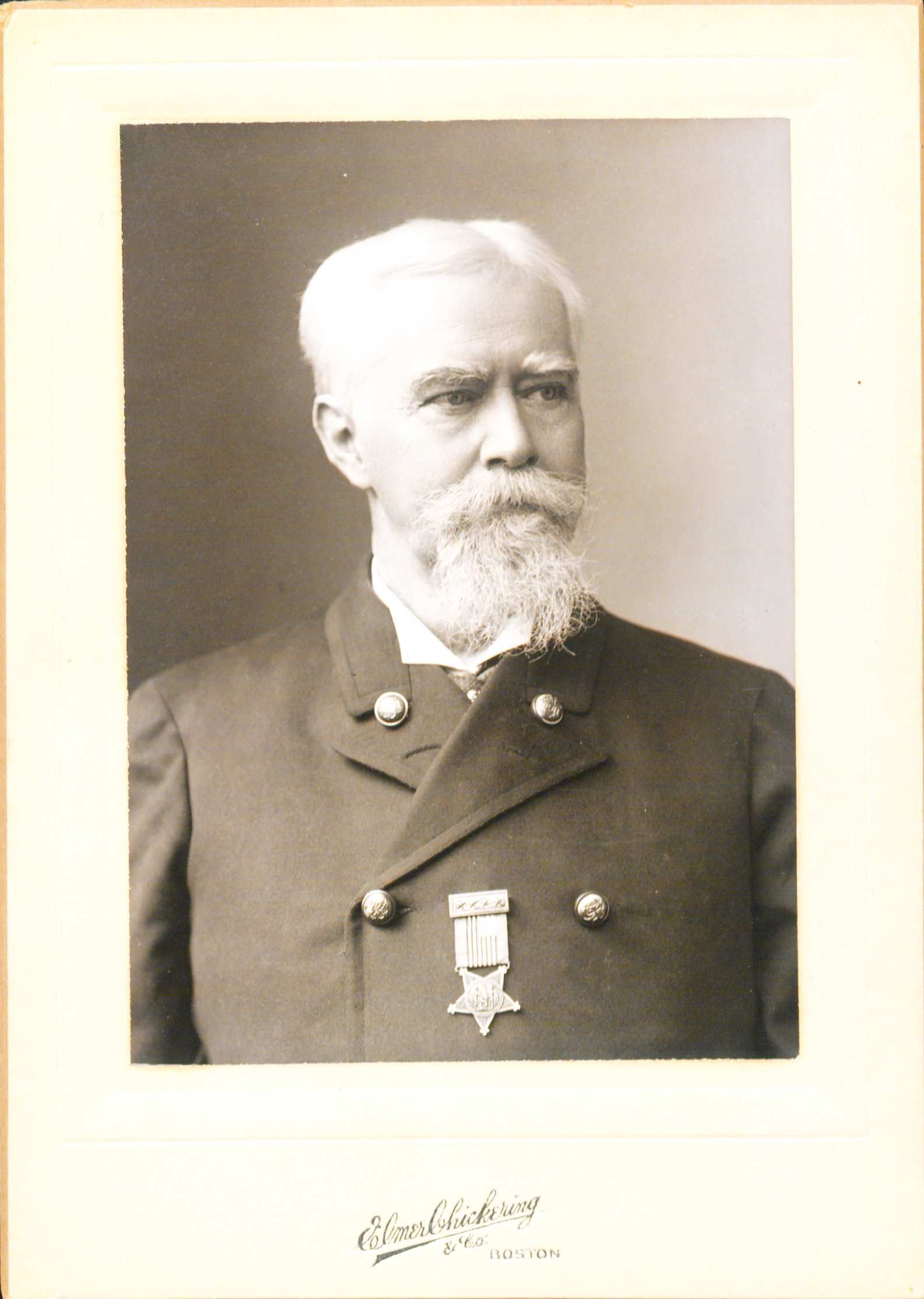 Portrait of John Black wearing an overcoat with a medal hanging in the middle of his chest. He is looking off to the eright