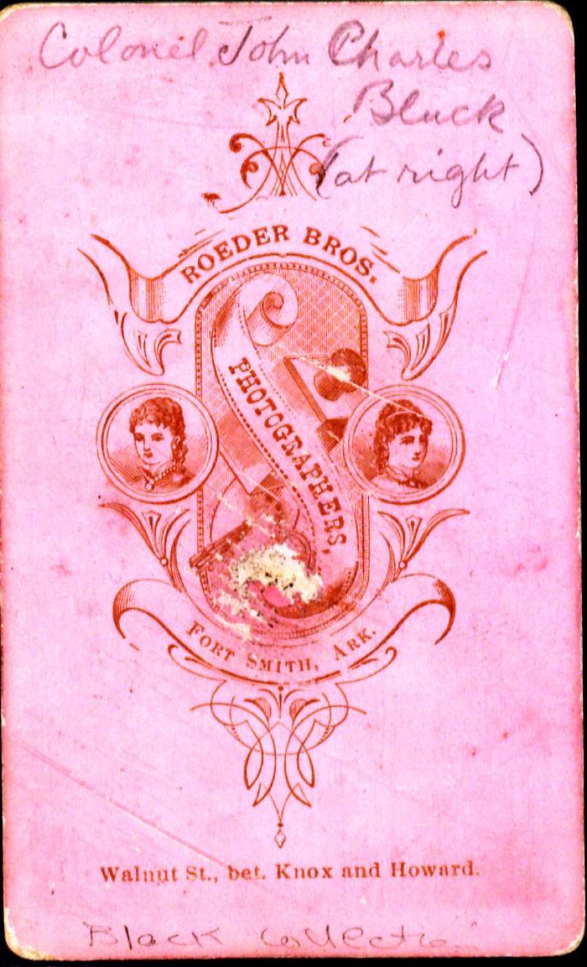 Pink background back of a photo with the photographers stamp. There are three faces on teh stamp