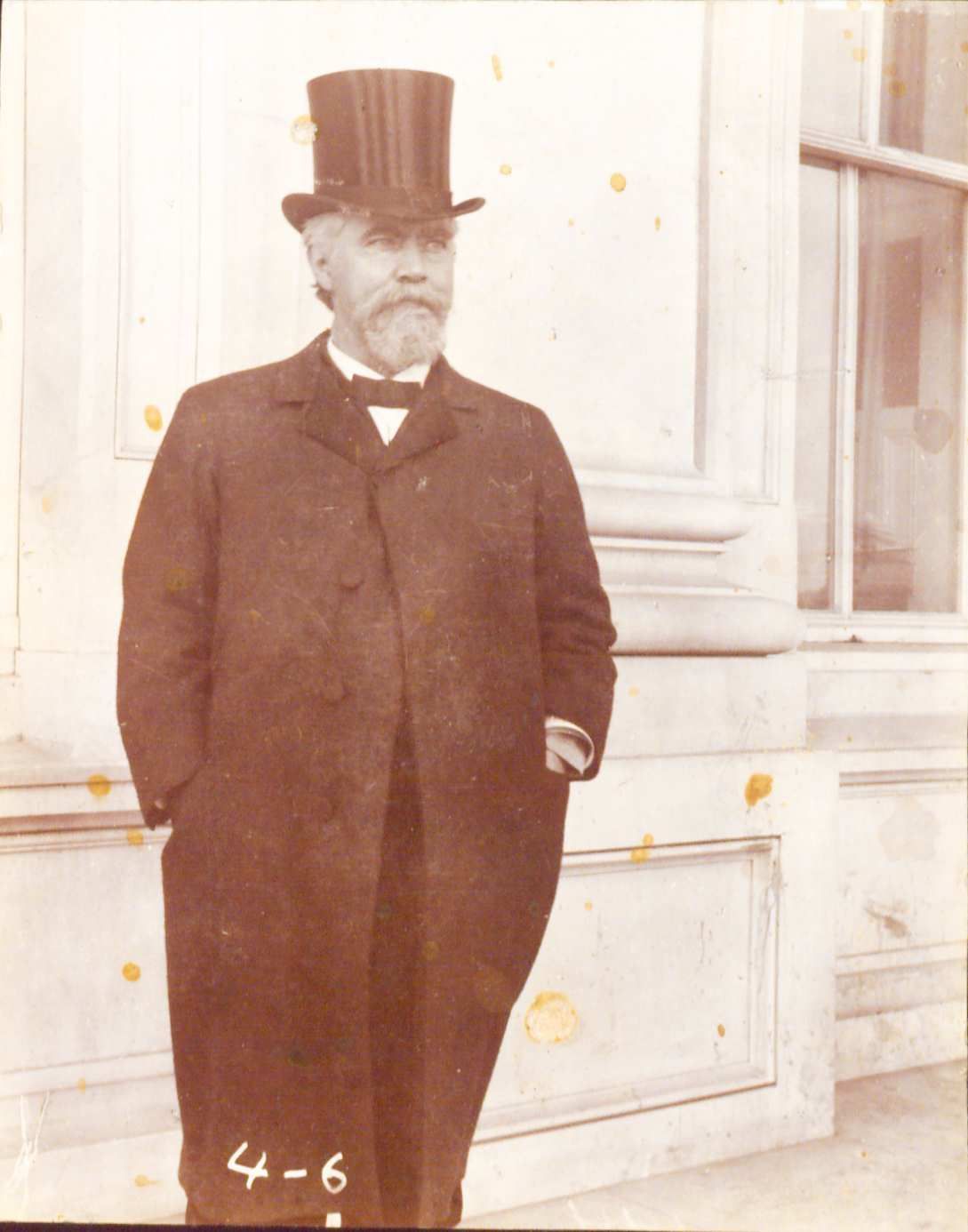 Picture of John Black standing otuside a building. He is wearing a hat and an overcoat
