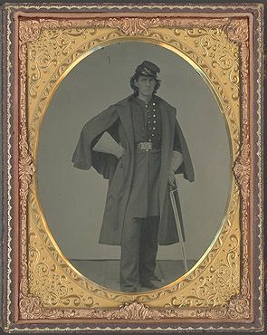Full body portrait of William Black in a military uniform. He is wearing a hat, an overcoat, white gloves. His uniform has buttons down the front and a belt buckle. His right hand is propped on his hip and he is holding a sword in his left hand. The sword is pointing towards the ground