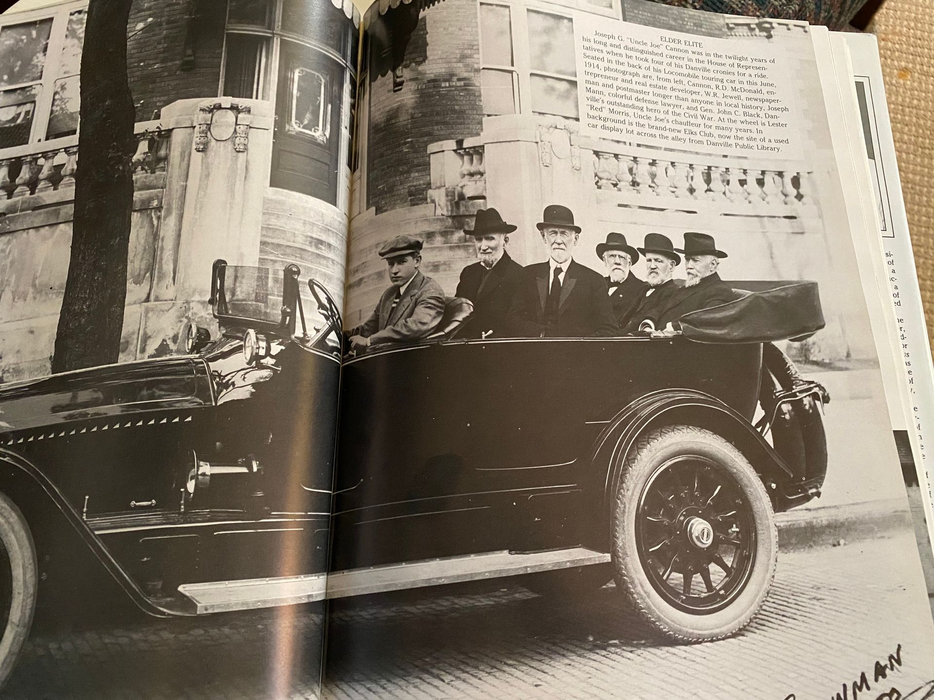 Picture of a newspaper or magazine clip of a car wtih 6 gentlemen sitting in an open top car. All are wearing hats and coats